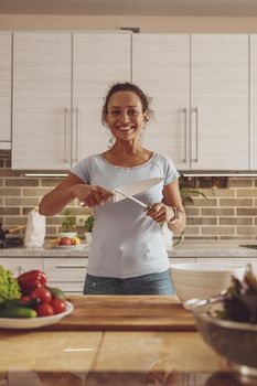 Housewife prepares to cut vegetables for a salad and sharpens a large knife standing in the kitchen