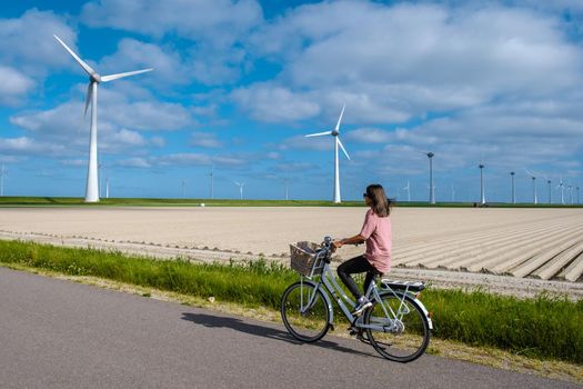 young woman electric green bike bicycle by windmill farm , windmills isolated on a beautiful bright day Netherlands Flevoland Noordoostpolder