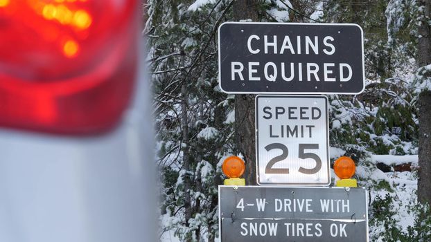 Chains or snow tires required traffic sign, mountains winter highway, Yosemite snowy forest, California USA. Icy road caution or warning, safety during snowfalls for transport. Speed limit in woods