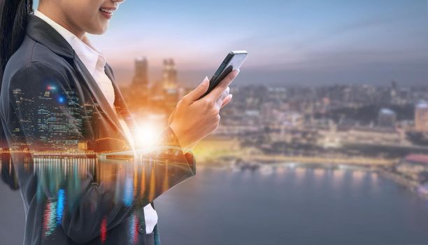 Young businesswoman using mobile phone with modern city buildings background. Future telecommunication technology and internet of things ( IOT ) concept.