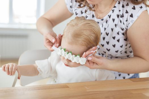 Mother helps her deaf baby daughter putting hearing aid in little girl's ear indoors - cochlear implant and innovative medical technologies