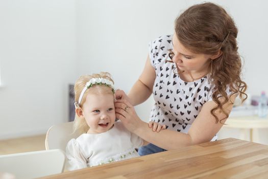 Mother helps her deaf baby daughter putting hearing aid in little girl's ear indoors - cochlear implant and innovative medical technologies