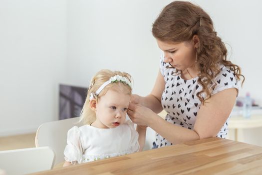 Mother helps her deaf baby daughter putting hearing aid in little girl's ear indoors - cochlear implant and innovative medical technologies