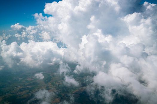 Earth landscape viewed from airplane. Earth surface under the white clouds and blue sky from aerial view. Cloudy weather covering residential land and argriculture land.