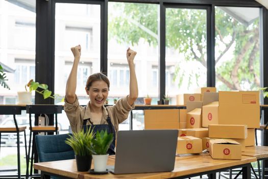 Happy young Asian woman entrepreneur, Smile for sales success after checking order from online shopping store in a smartphone at home office, Concept of merchant business online and eCommerce.