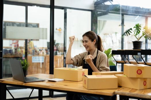 Happy young Asian woman entrepreneur, Smile for sales success after checking order from online shopping store in a smartphone at home office, Concept of merchant business online and eCommerce.