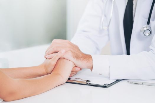 Male doctor soothes a female patient in hospital office while holding the patients hands. Healthcare and medical service.