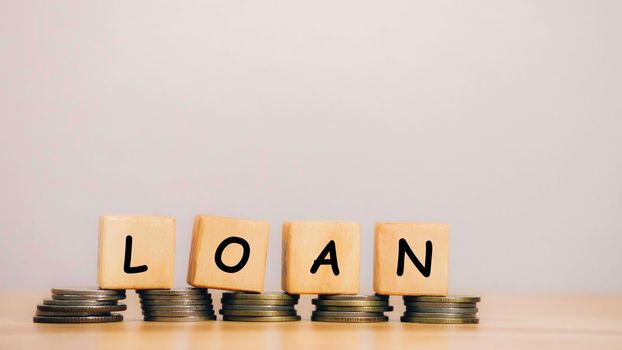 Close Up wooden block written LOAN against on stack coins to business and finance concept. Fees and Interest from loans are main revenue for banks. Loans can be unsecured such as credit card.