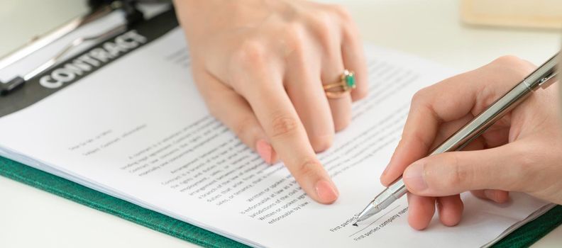 Businesswoman signs agreement contract with another businesswoman at the office. Close up shot at the woman's hand. Concept of business partnership and legal activities of lawyer.