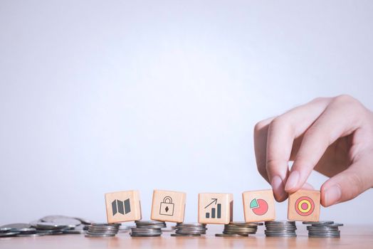 Hand of business strategy or e-commerce taking wooden blocks with target, padlock and graphs icons laying on stack coins or real money  .Business achievement goal,growth success and benefits concept.