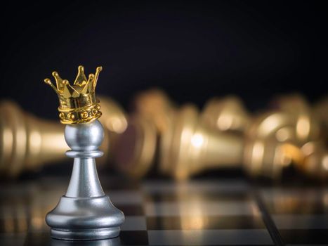 A silver pawn standing crowned in battle chess game on board with gold chess background. To fighting with teamwork to victory, business strategy concept and leader and teamwork concept for success.