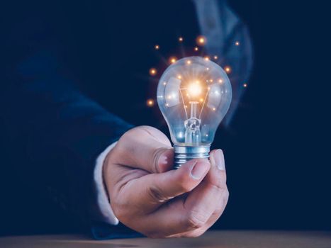 Hand of businessman holding light bulb with fire spark shine glitter for new idea with innovation and inspiration, communication and technology in science concept.