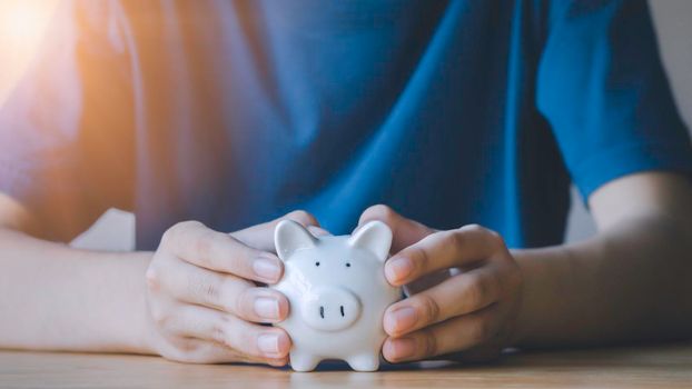 Portrait of teen boy holding and giving white piggy bank in garden. Concept for saving money, loan, property ladder, financial, real estate investment and bonus.