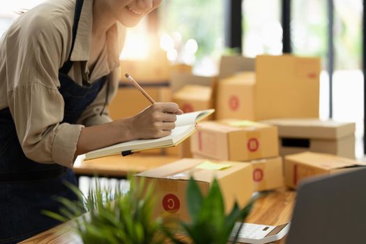 Startup SME small business entrepreneur SME or freelance Asian woman using a laptop with box, online marketing packaging box and delivery, SME concept.