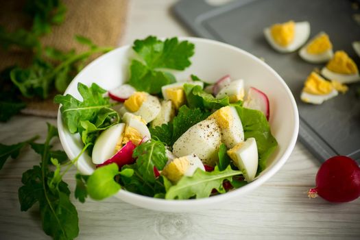 Fresh spring salad with fresh lettuce leaves, radishes, boiled eggs in a bowl on a wooden table