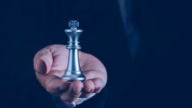 Hand of businessman holding the silver king chess to fighting to play successfully in the competition with Strategy, leadership and management ideas concept.
