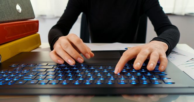 Female hands typing on laptop while sitting at office desk indoors. Woman fingers typing and texting on computer keyboard while working online, writes mails.