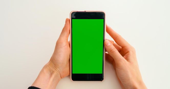 Green Screen Mock-up Chroma Key smartphone. Watching photo content, blogs, POV. Close-Up of Woman Hands are holding vertical smartphone with Green Screen on yellow background.