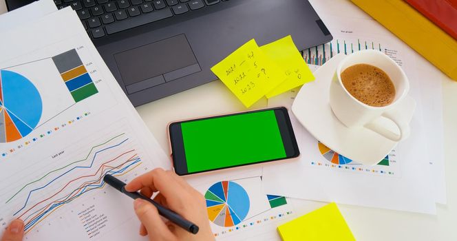 Top view of Green Screen Mock-up Chroma Key of smartphone during analysis of financial reports, worksheet. Business office.