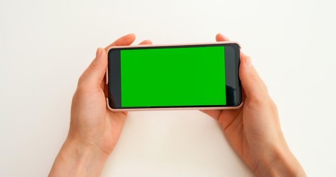 Green Screen Mock-up Chroma Key smartphone. Watching photo content, blogs, POV. Close-Up of Woman Hands are holding horizontal smartphone with Green Screen on yellow background.