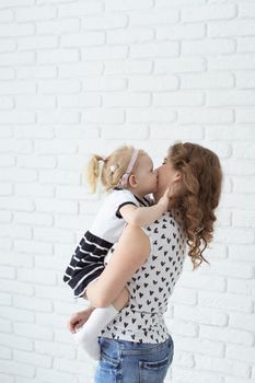 Mother helps her deaf baby daughter putting hearing aid in little girl's ear indoors - cochlear implant and innovative medical technologies