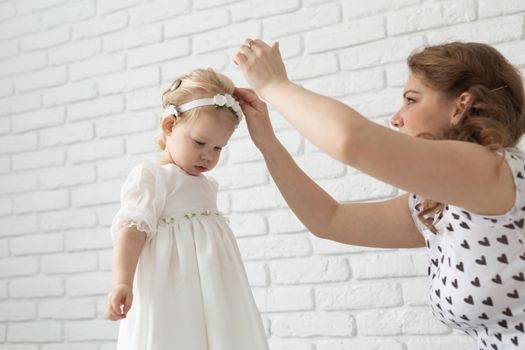 Mother helps her deaf baby daughter putting hearing aid in little girl's ear indoors - cochlear implant and innovative medical technologies