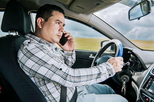 A man driver calling on the phone in his car, concept of man calling on the phone while driving, Side view of a young man sitting inside car using mobile phone