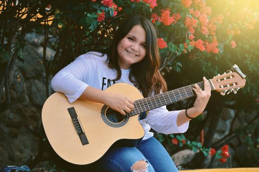 A girl sitting playing guitar outdoors, Portrait of a smiling girl playing guitar, Lifestyle of a girl playing guitar outdoors