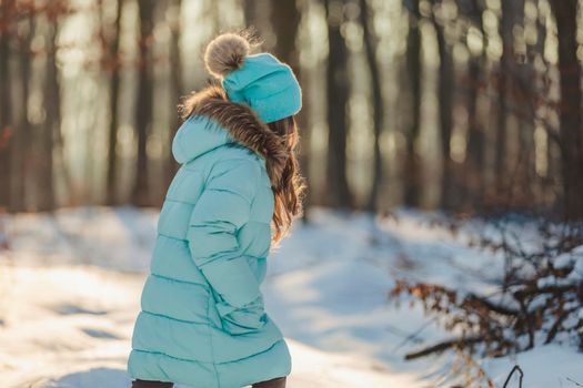 girl in a jacket and hat of turquoise color against the backdrop of a snowy forest