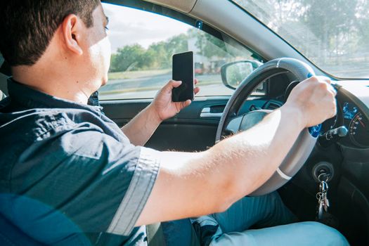 Person holding the cell phone and with the other hand the steering wheel, Man using his phone while driving, Concept of irresponsible driving, Distracted driver using the cell phone while driving
