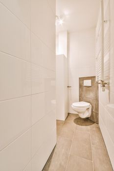 Wall hung toilet and small sink in corner in lavatory room with beige tile