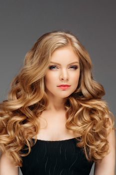 Studio fashion portrait of attractive sensual young woman with long wavy fair hair and blue eyes looking at camera. Natural beauty concept. Caucasian.