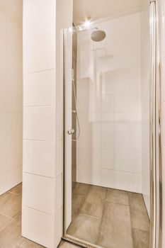 Shower faucets attached to tiled wall near glass partition and ornamental curtail in washroom at home