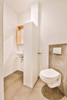 Wall hung toilet and small sink in corner in lavatory room with beige tile