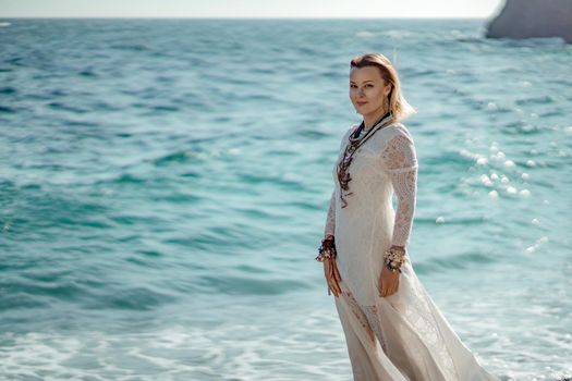 Middle aged woman looks good with blond hair, boho style in white long dress on the beach decorations on her neck and arms