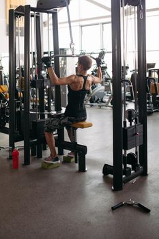 View of fit and sporty young woman doing thrust of upper block to chest by hands in gym. Fit girl in black with big muscles working. Sport lifestyle.