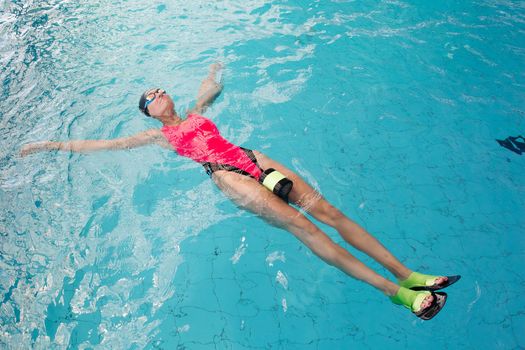 View of sporty woman in goggles and cap swimming in the blue water pool. Athletic girl concentrated swimming, wearing in pink swimsuit, engaged in sports. Concept of water sport and activities.