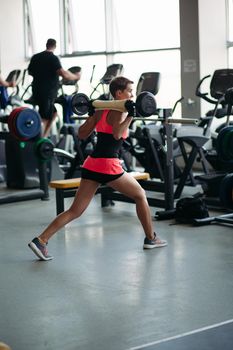 Back view of sporty woman with short hair wearing in pink working at gym alone and looking away. Fit woman doing exercise with barbell. Sportlife concept.