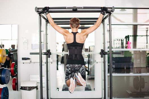 Rear view brunette woman with short hair, doing workout tightening on bar. sporty and strong girl with athletic body doing exercises on bar in gym. fit concept.