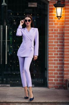 Portrait of a business lady with a determined look in black glasses and on rebounds. The girl is dressed in a strict pale purple suit. Isolated against the background of the building. Business woman concept.