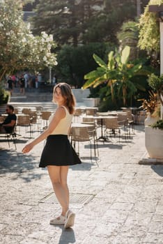 Girl tourist walking through ancient narrow street on a beautiful summer day in MEDITERRANEAN MEDIEVAL CITY , OLD TOWN bUDVA, MONTENEGRO. Young beautiful cheerful woman walking on old street at tropical town. Pretty girl looking at you and smiling