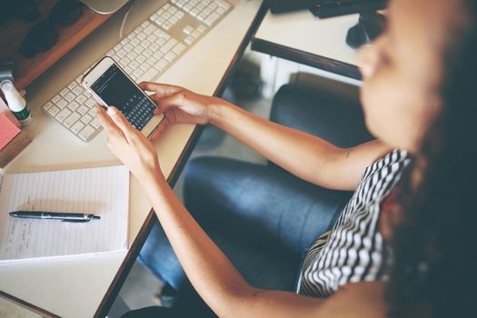 Shot of an unrecognizable young woman sitting alone and using her cellphone to work from home stock photo