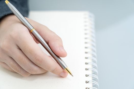 Businesswoman writing on notebook in office, hand of woman holding pen with writing notebook on desk