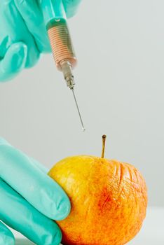 A hand in a medical glove inserts a syringe into apple. Harmful food additives. GMOs Concept. Injecting on apple at laboratory. Fruit genetic modification concept.