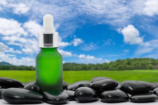 Serum oil bottle dropper mock up or essential oil with black stone agent green grass field and blue sky