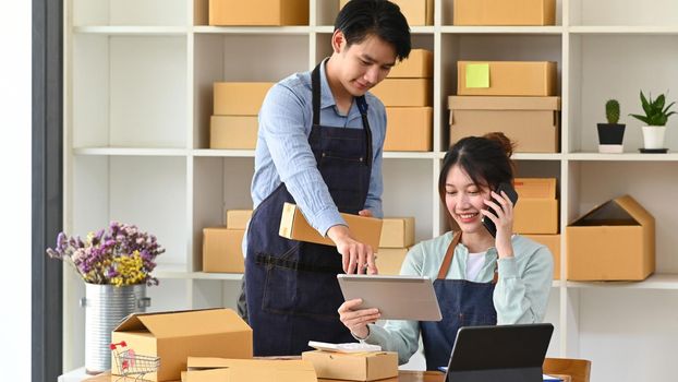 Young Asian couple starting their own small business at home office. Online selling, e-commerce concept.