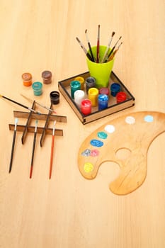 Wooden palette with laying on paints and cup with paintbrushes on the desk