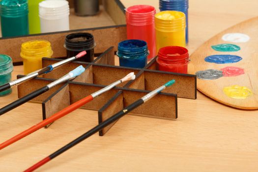 Wooden palette and box with colorful paints and paintbrushes on wooden table