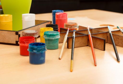 Paintbrushes and motley paints in cups on wooden table Selective focus
