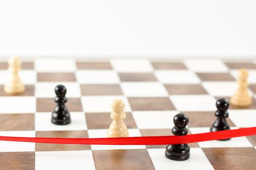 Black pawn's figure crossing the red finish ribbon. Chess leadership and success concept